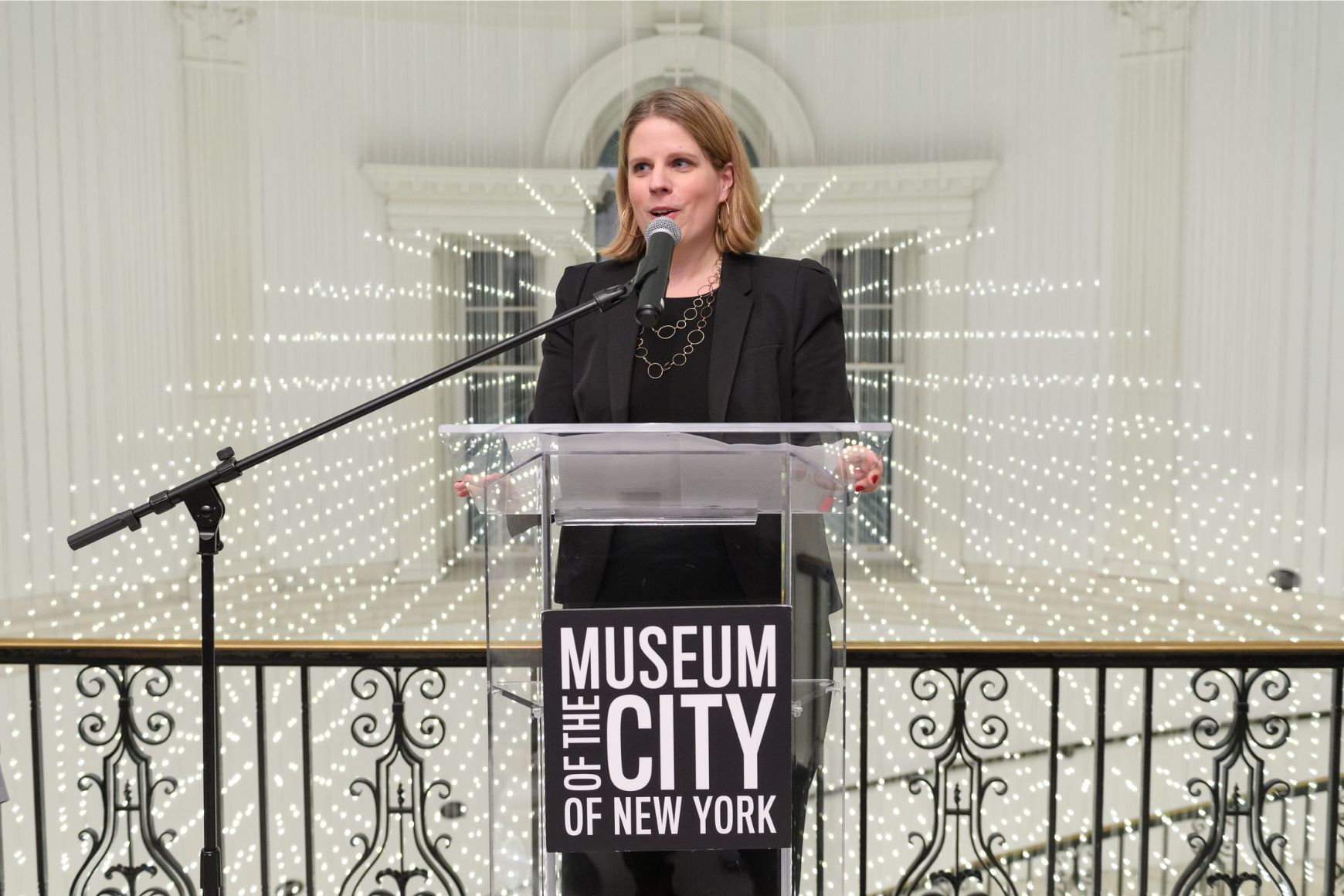 Image of curator Lilly Tuttle at clear podium with text logo "Museum of the City of New York"